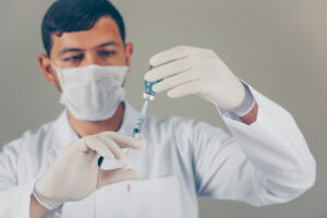 Doctor with gloves and mask unfilling the syringe into a vial on gray background. side view horizontal Doctor with gloves and mask unfilling the syringe into a vial on gray background. side view horizontal